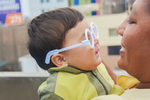 young boy wearing eyeglasses being held by his mother, both smiling