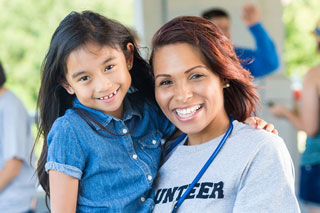 community volunteer holding a young hispanic girl, both smiling