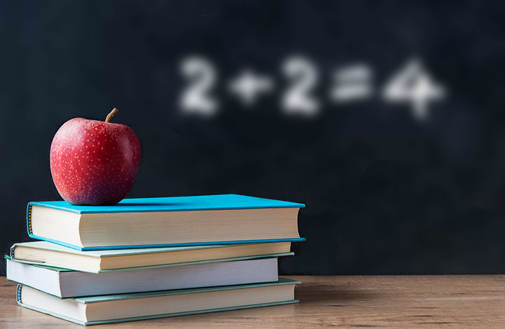 Sharp, clear image of a stack of books with an apple on top, and a blurred image of a chalkboard in the background, demonstrating myopic vision.